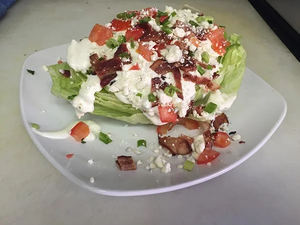 Wedge salad with bleu cheese crumbles, bacon and tomato